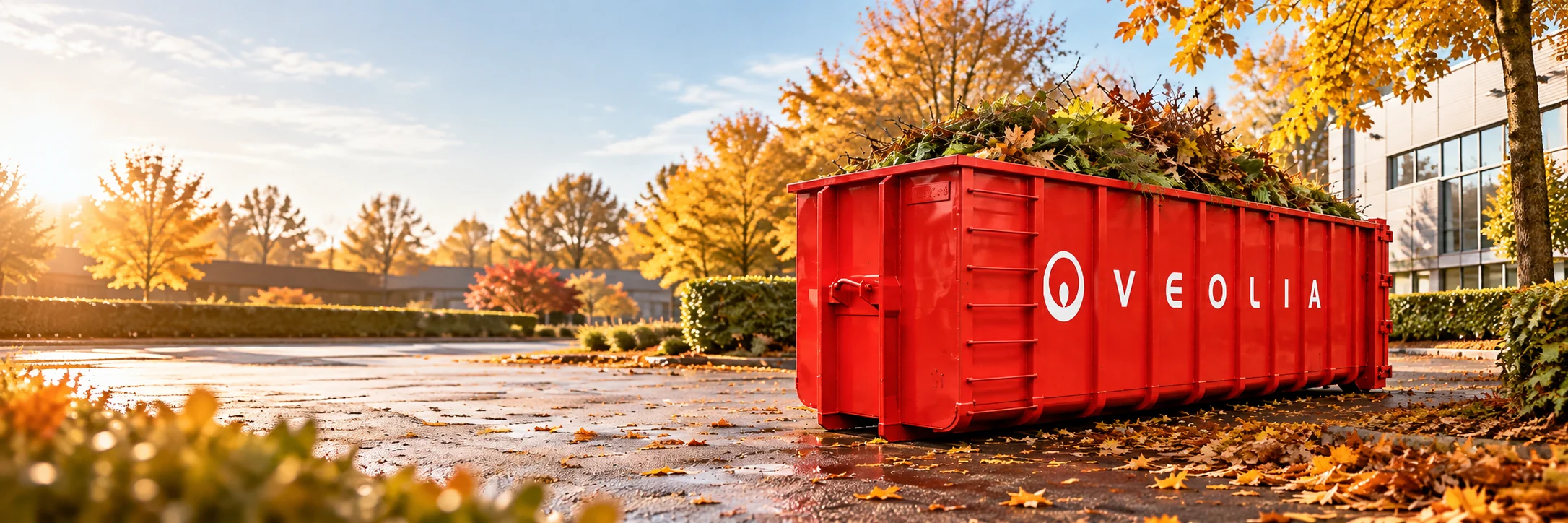 Conteneur ouvert rouge Veolia rempli de feuilles mortes et de déchets de taille sur un site professionnel en automne